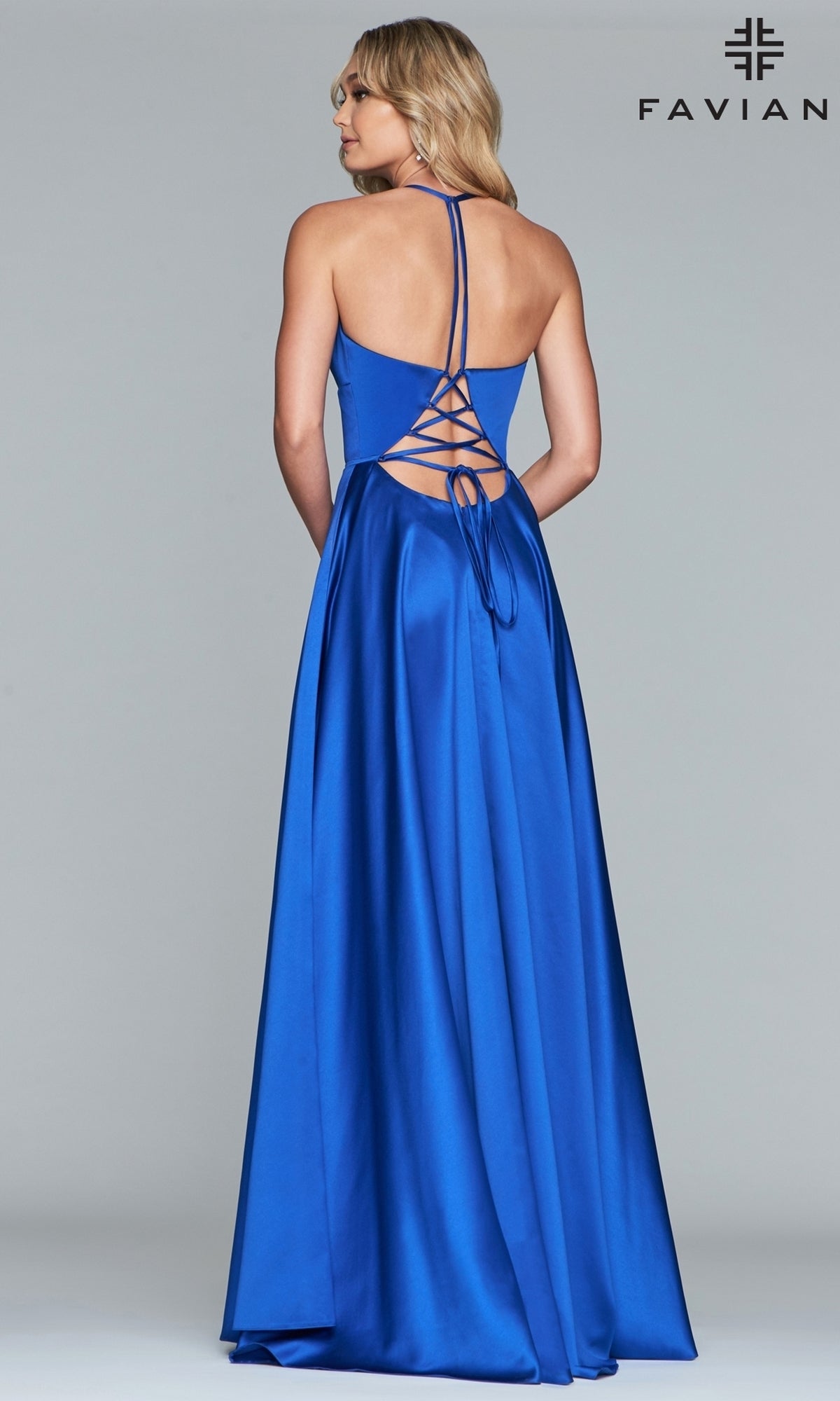 A woman in the Corset-Back A-Line Long Satin Prom Dress by Faviana, featuring royal blue satin and a lace-up open back, stands against a plain light gray background. The